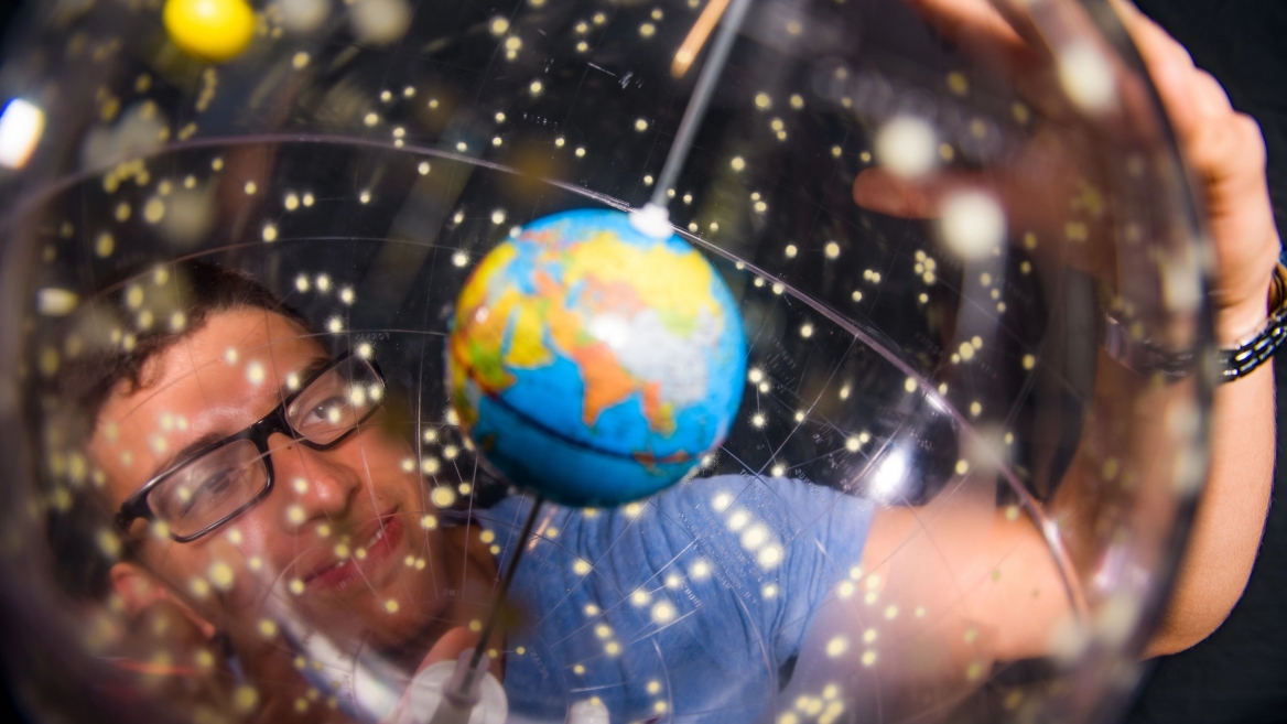 Person wearing glasses looking at a small globe.