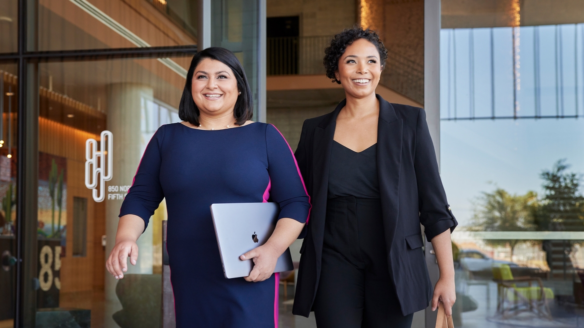 Two women in business attire walk out of a building
