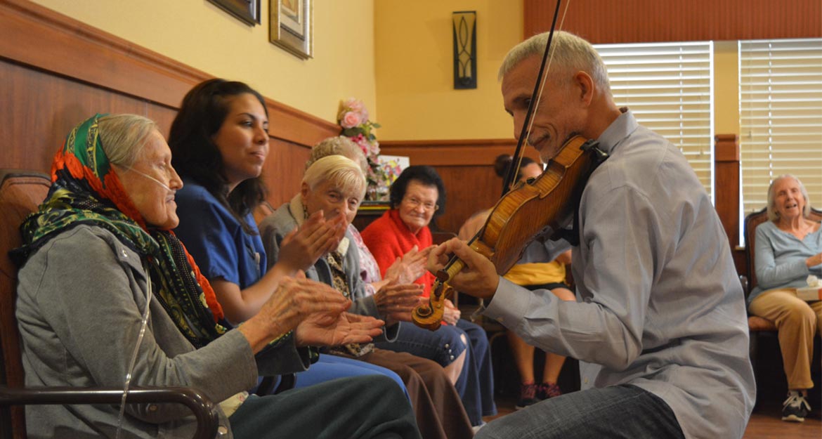 man playing violin to elderly woman