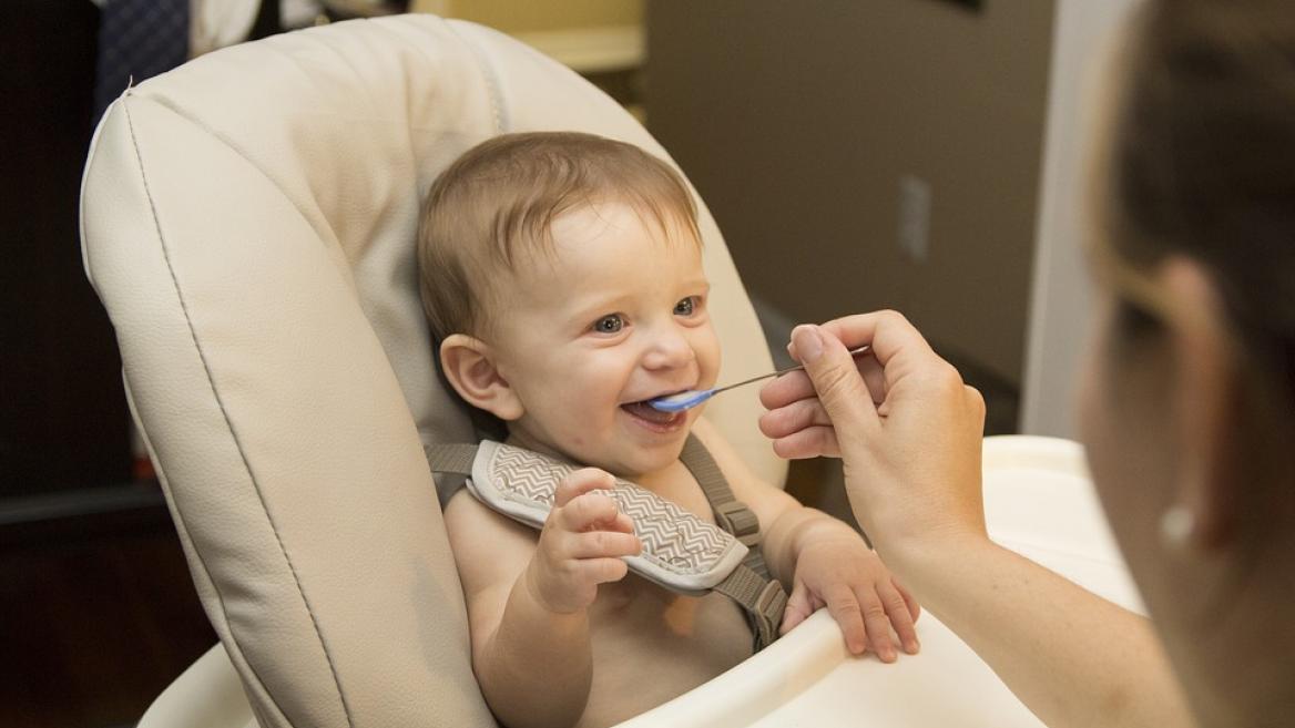 baby in high chair being fed by mom with a spoon