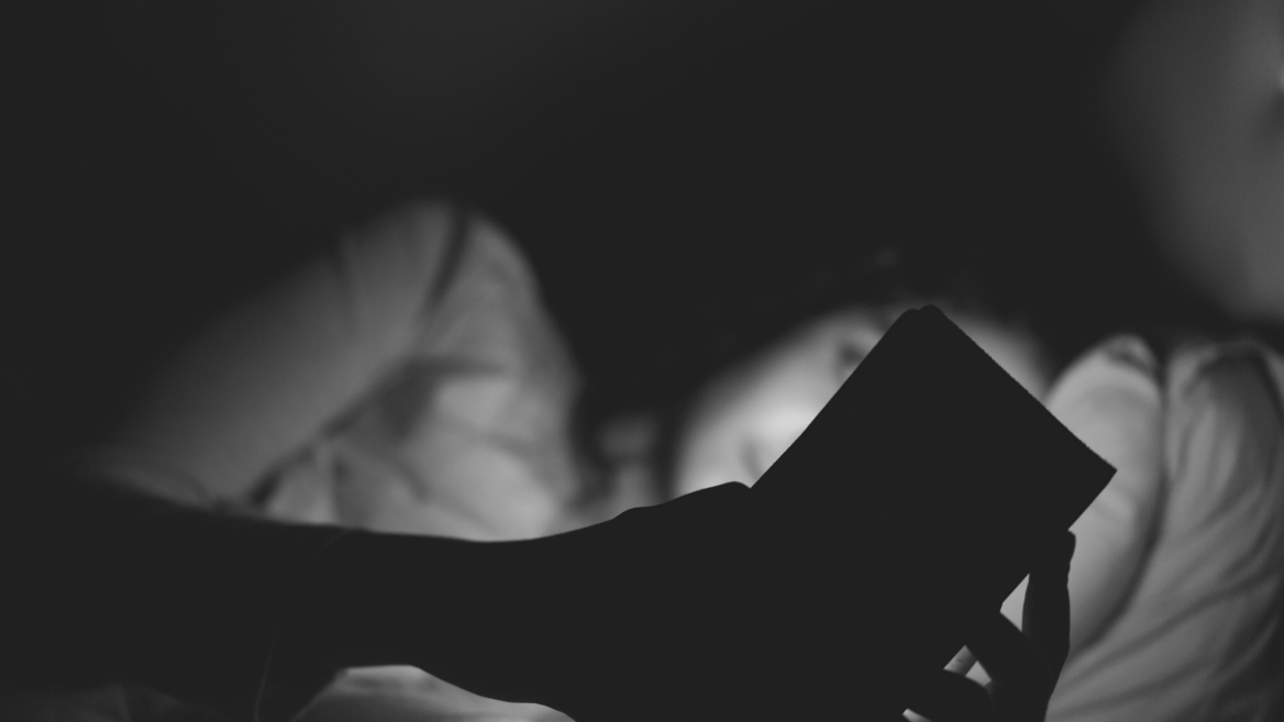 A woman lies in bed scrolling her device because she can't sleep. The image is in black and white.