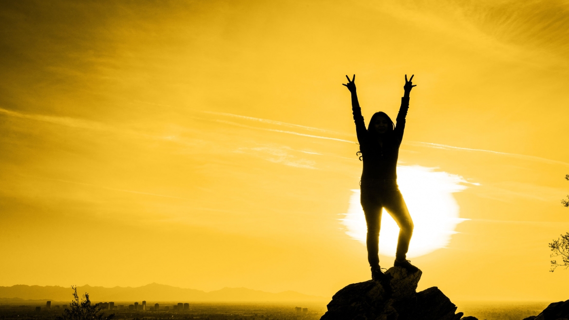 woman on mountain with sun behind her making pitchforks with hands